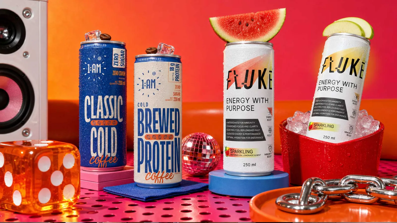 Two 1:AM coffee cans and two Fluke sparkling cans styled with ice, fruit and props on a pink set