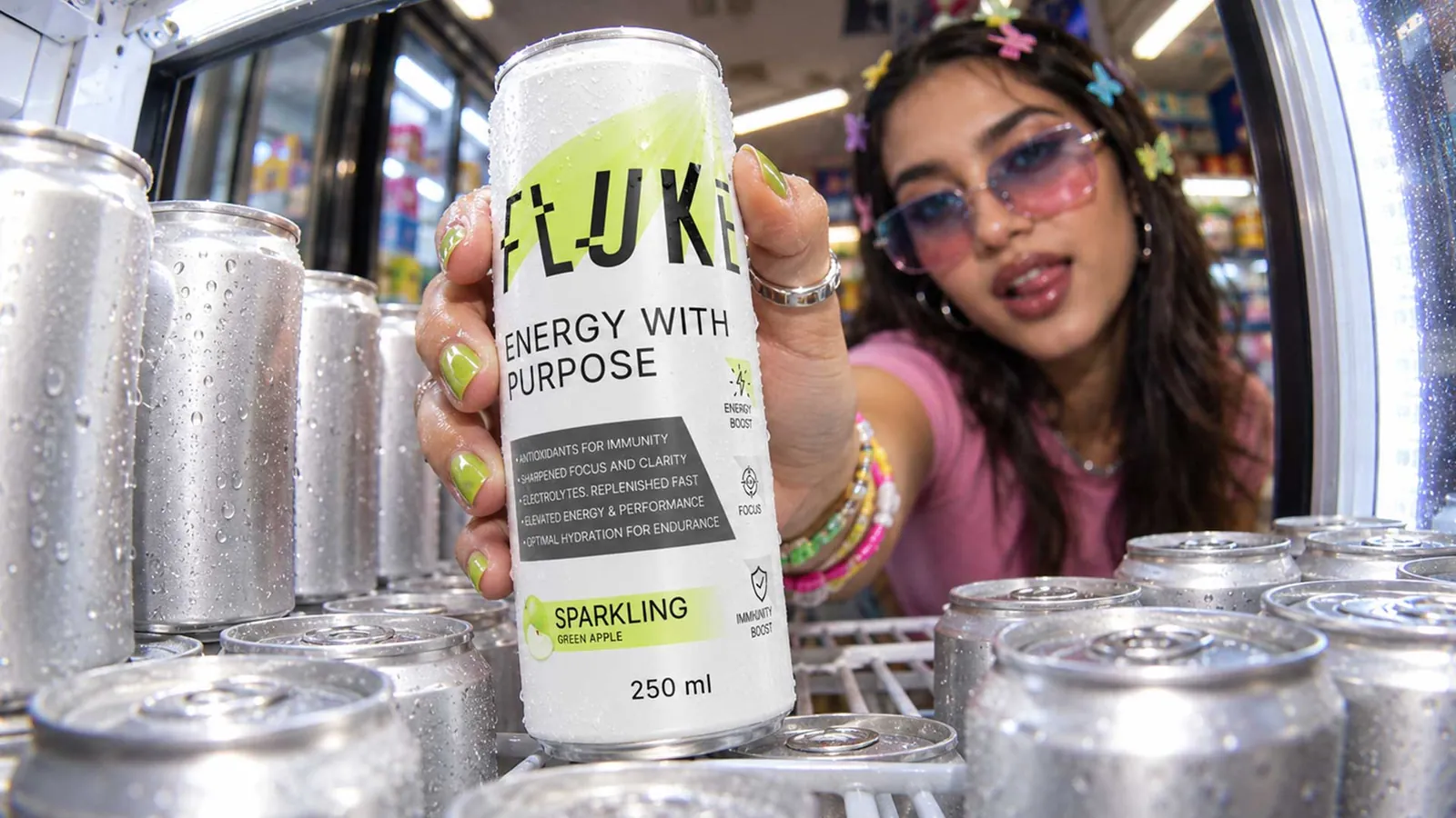 Hand taking a Fluke Sparkling Green Apple can out of a glass-door fridge lined with chilled cans
